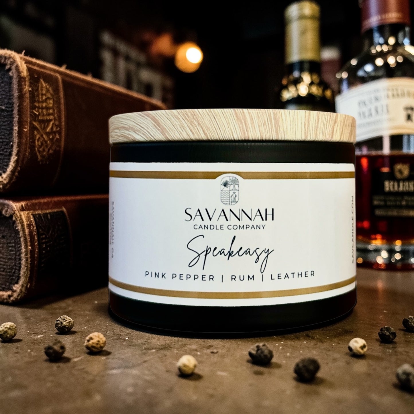 Savannah Candle Company candle with peppercorns on a leather book with a glass of rum in the background.