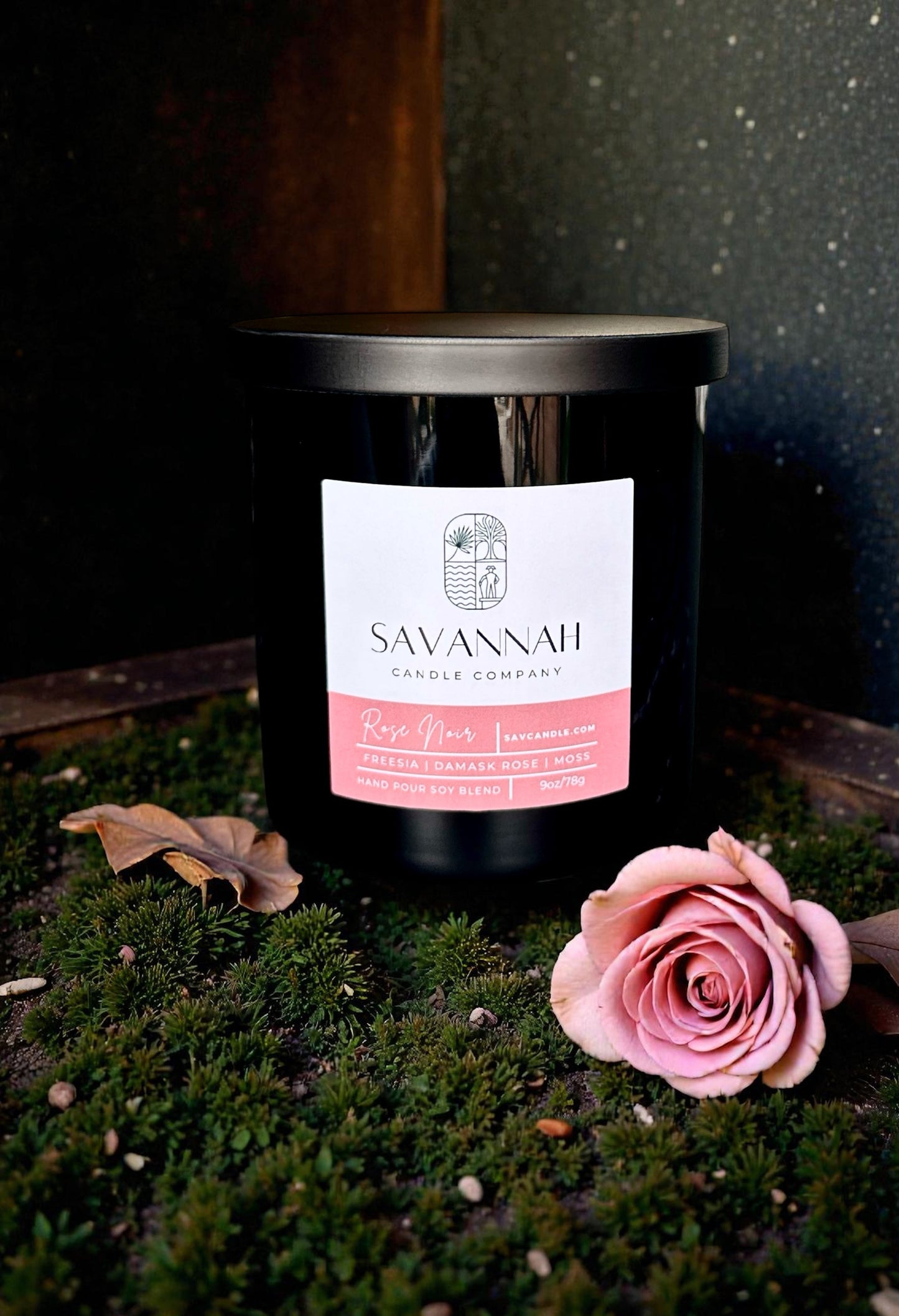 Savannah Candle Company candle with a pink rose on a dark background. Rose and moss fragrance.