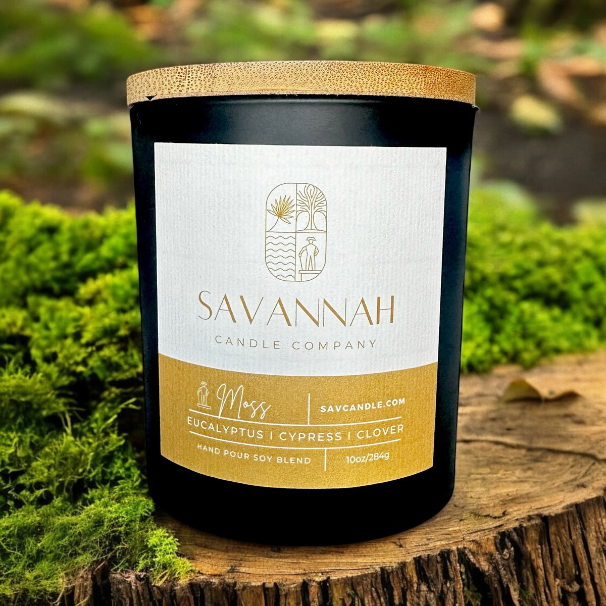 A candle sitting on a tree stump with green moss in the background. The candle smells like pine, fir, and clover. this is a fresh and clean scent that smells like the outdoors and grass Mixed with pine.