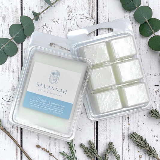 Two packaged wax melts from Savannah Candle Company, one labeled 'Marsh', displayed on a white rustic wood background with green eucalyptus leaves.