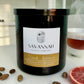 Black candle jar with 'Savannah Candle Company' label on a white surface with spices and a fruit slice. The candle name is veranda, and the fragrance is cardamom, black tea, and grapefruit.