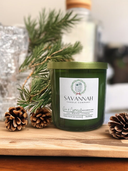 Savannah Candle Company candle with pine branches and pinecones on a wooden surface.  The fragrance is Frasier fir.  Named gin and cypress 
