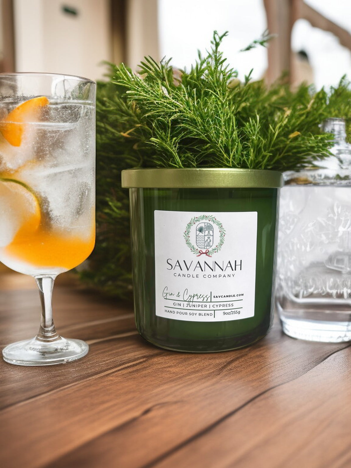 Savannah Candle Company candle on a table with a glass of iced gin and a cypress branch.  The candle fragrance is Gin and Cypress.