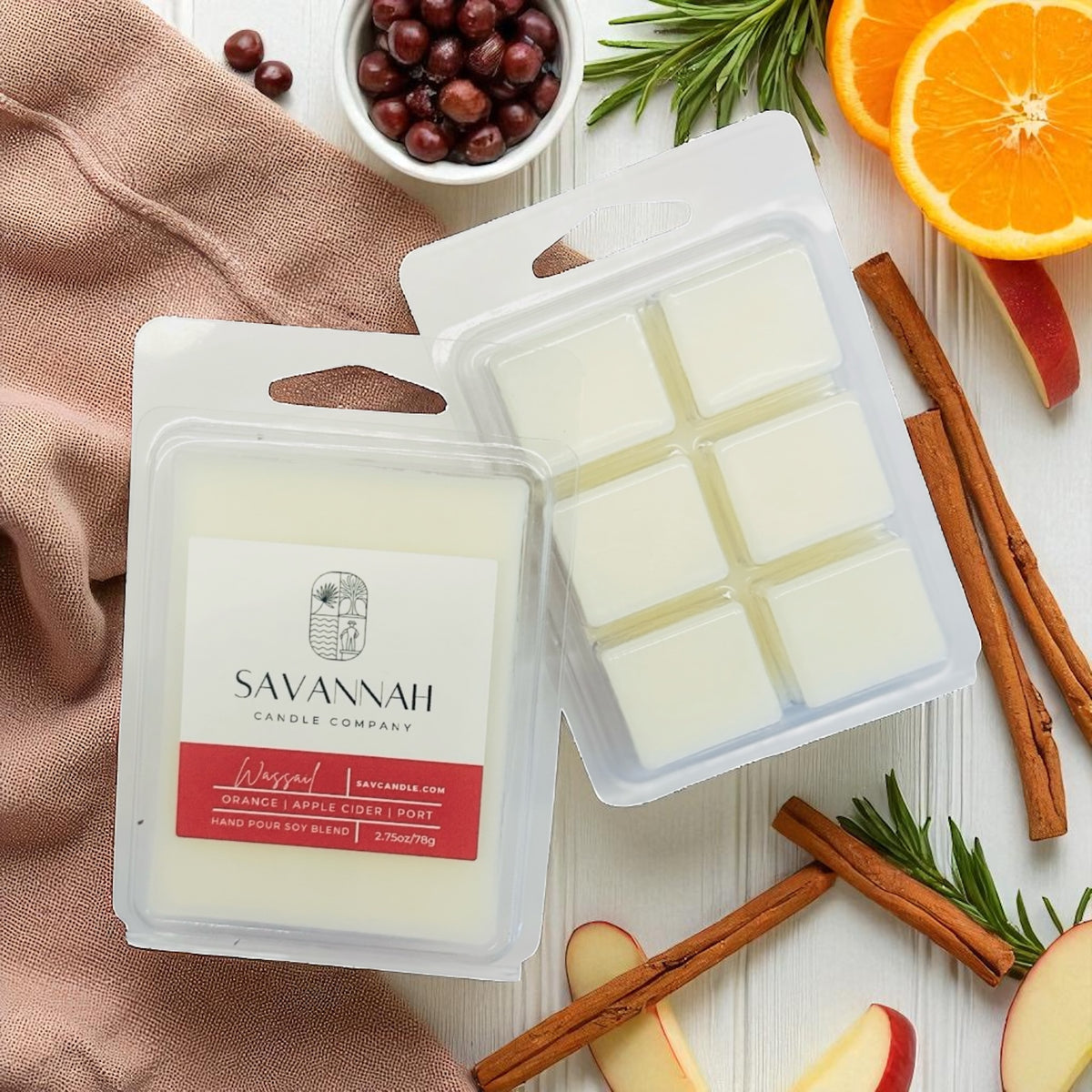 Savannah Candle Company wax melts with cinnamon sticks, apples, and oranges on a wooden surface.