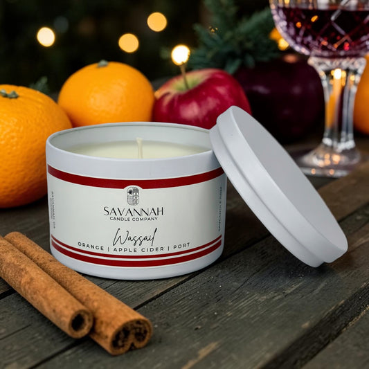 A white candle tin with its lid leaning beside it on a rustic wooden surface. The label reads Savannah Candle Company and Waspal Orange | Apple Cider | Port.